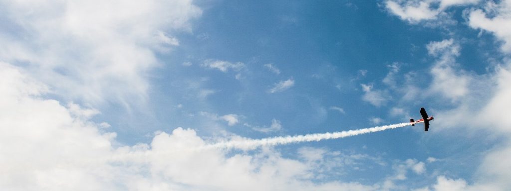 A small airplane leaves a trail of exhaust on a partly cloudy day