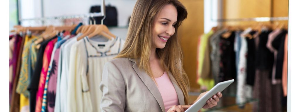 A smiling female looking at a tablet inside a clothing store